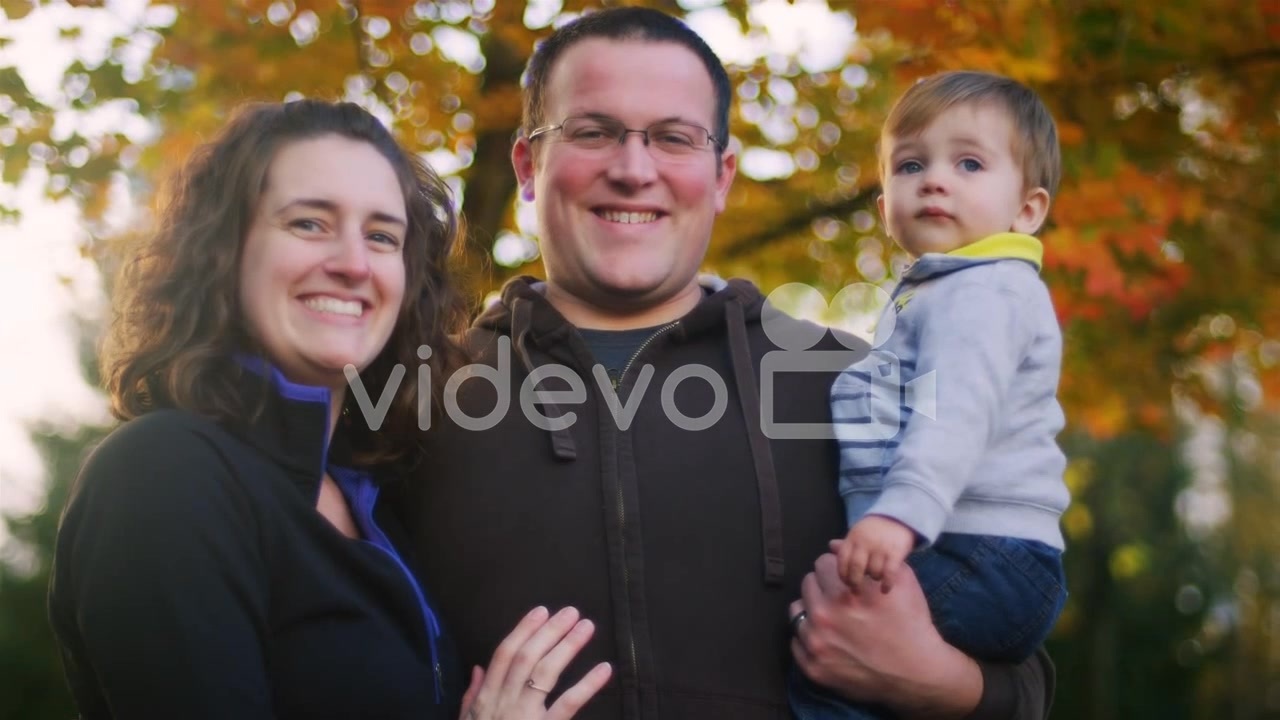 Family of three posing for a photo in front of a tree